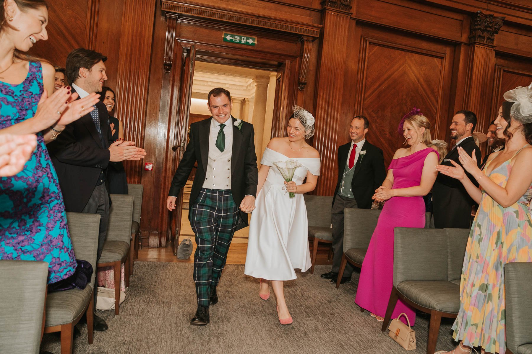  Bride and groom enter their wedding in The Westminster room at Marylebone Town Hall, to their family and friends clapping. 