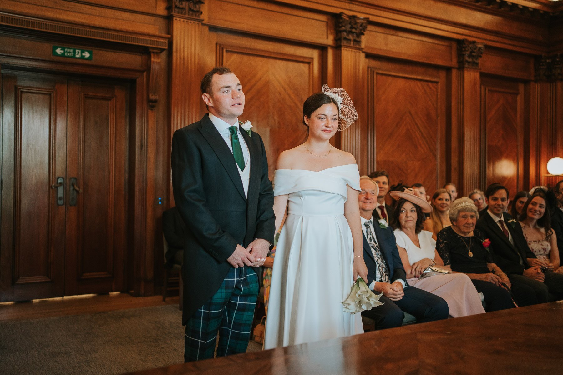  Bride and groom hold hands in The Westminster room at Marylebone Town Hall, in front of their family and friends. 