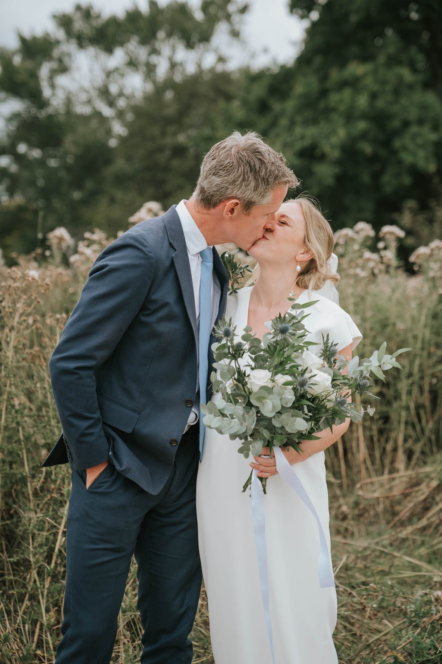  Groom and bride holding wedding bouquet kiss in Morden Park House gardens. 