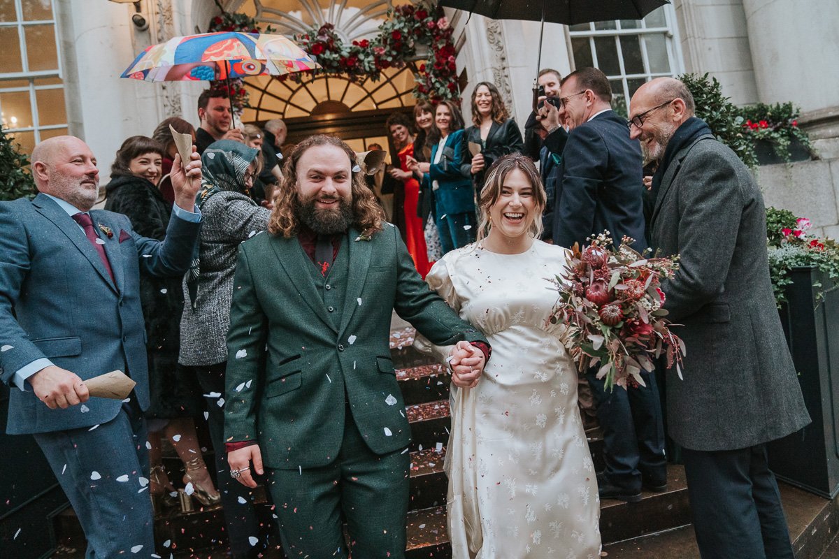  Bride and groom exiting Chelsea Old Town  Hall register office through their friends and family in the rain. 