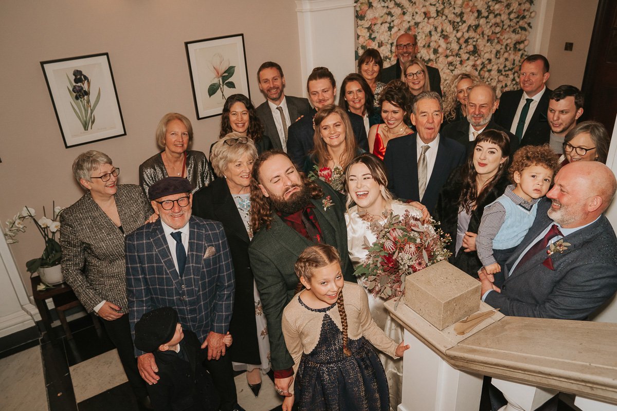  Bride and groom stand with their friends and family in the waiting room at Chelsea old Town hall. 