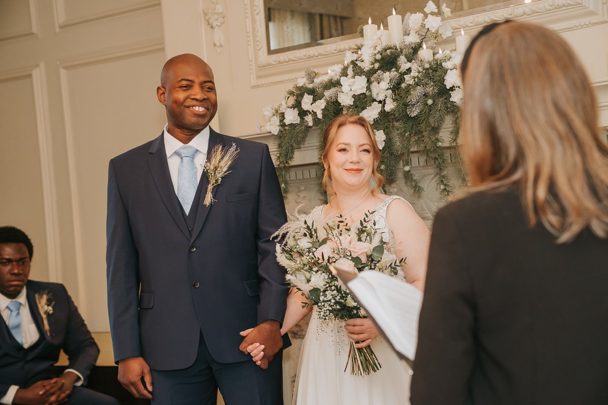  A bride and groom stand hand in hand and look at the registrar as she conducts the wedding ceremony in the pimlico room at marylebone town hall. 