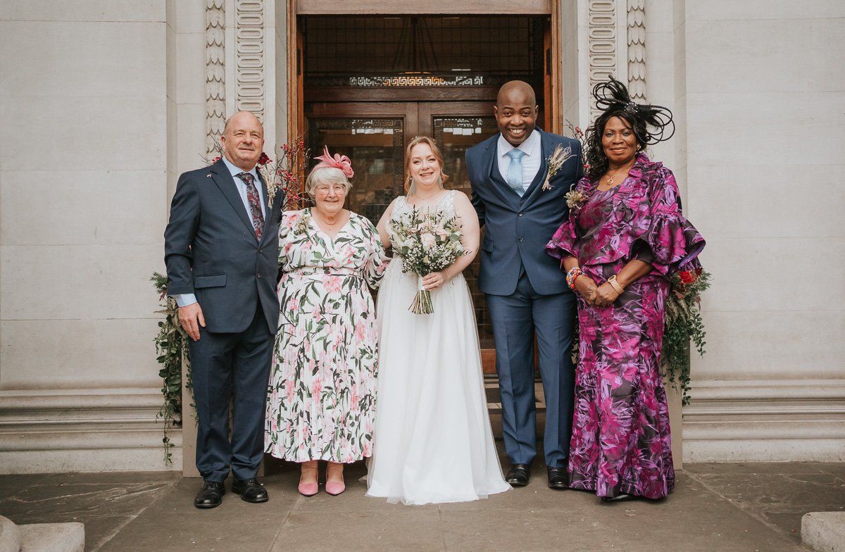  Newly married bride and groom pose with their mums and dads on the steps outside marylebone town hall register office. 