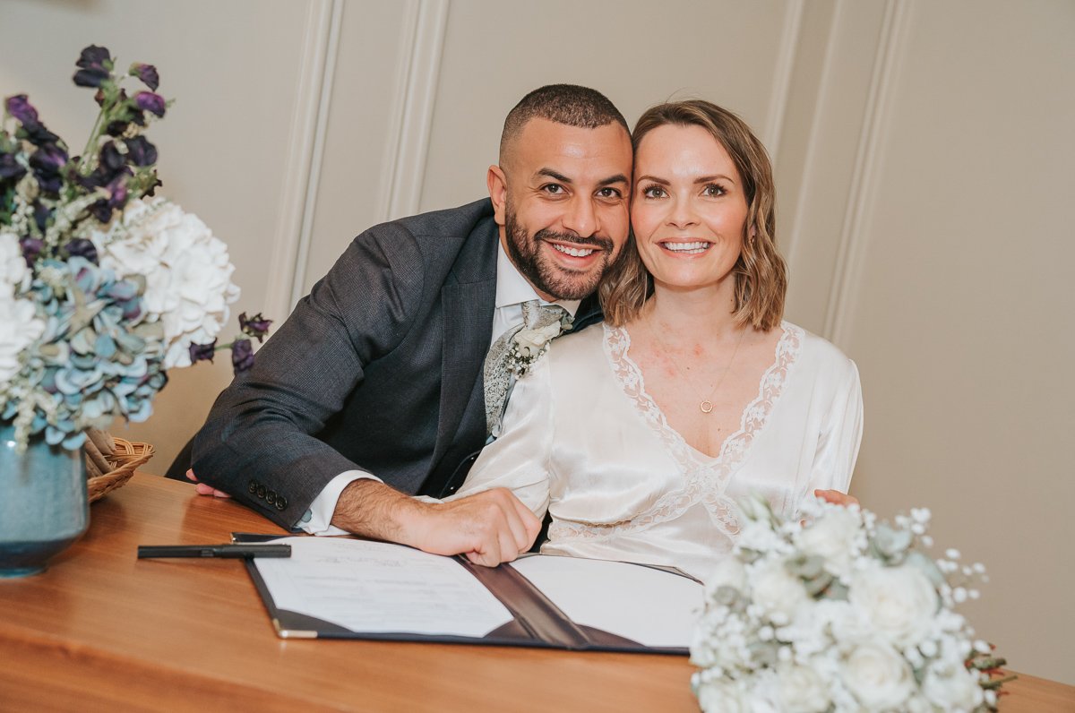  Smiling bride and groom sign the register after their wedding at marylebone town hall register office. 