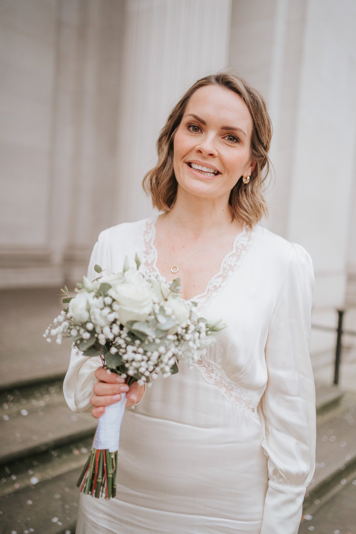  Radiant bride stands outside marylebone town hall holding her wedding flowers. 
