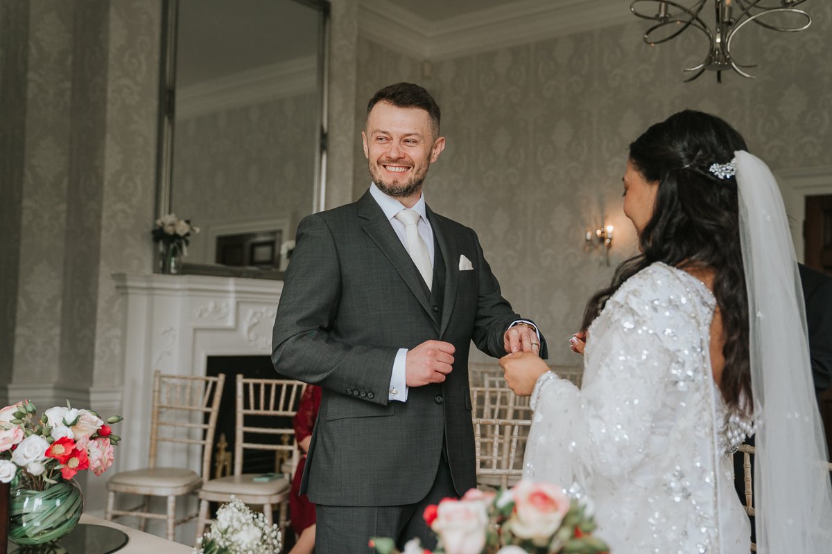  Groom puts ring on bride's finger during wedding at morden park house. 