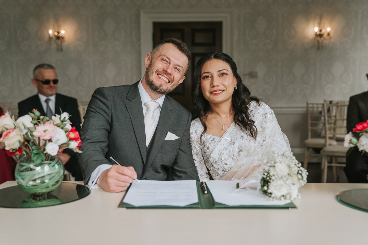  Bride and groom sit side by side after signing register at morden park house. 