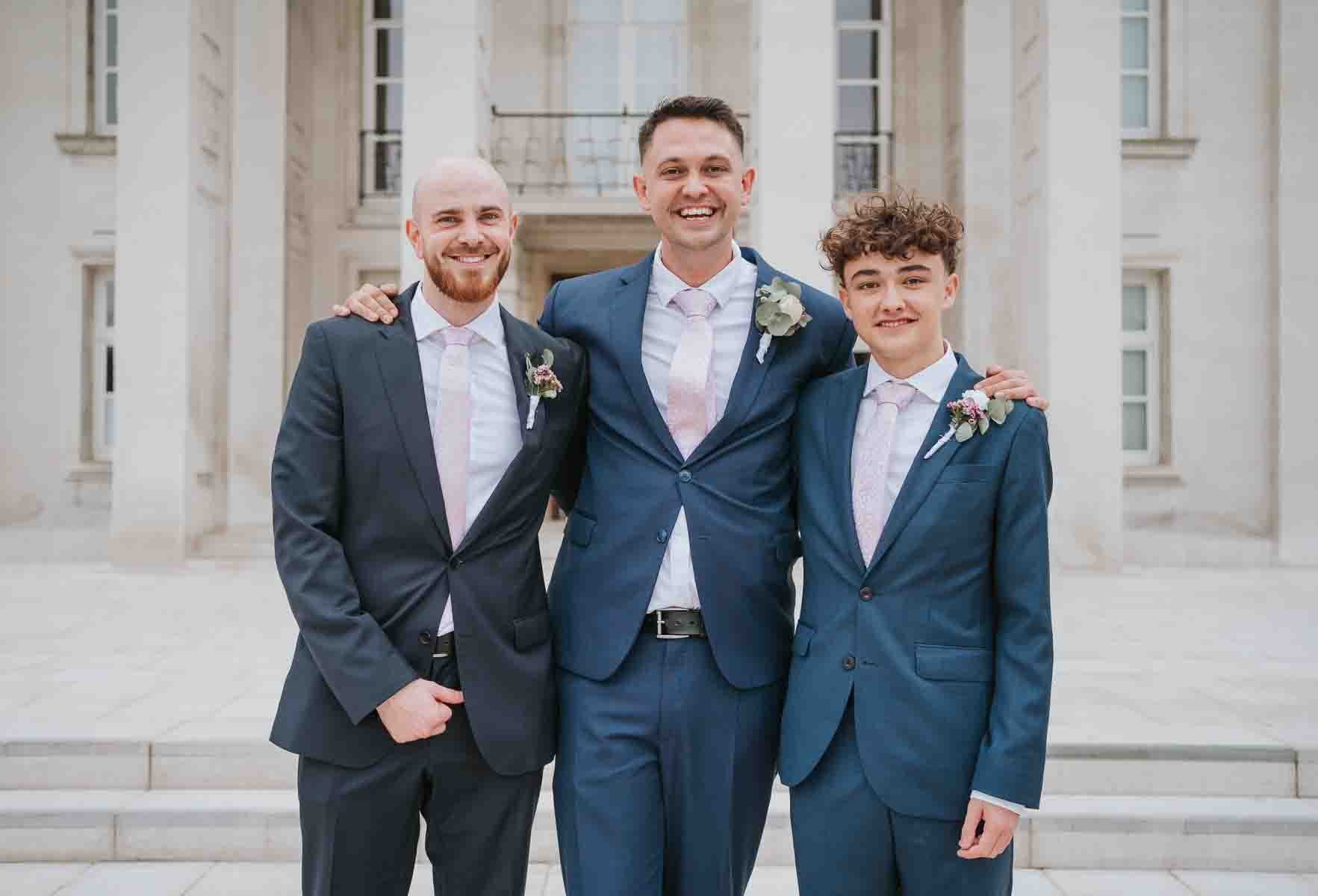  Groom, best man and groom's son stand outside the front entrance of Waltham Forest Town Hall. 