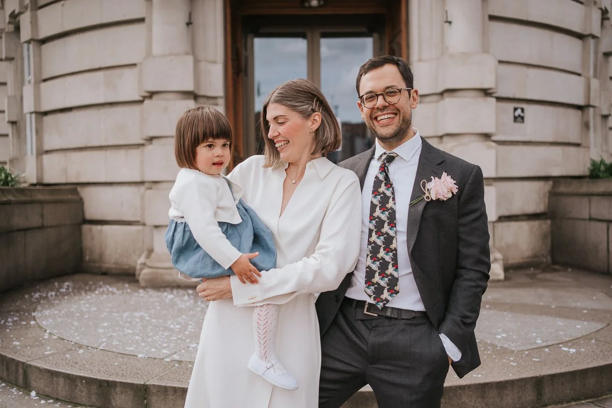  Bride and groom pose for photograph with young daughter outside front entrance of lambeth town hall. 