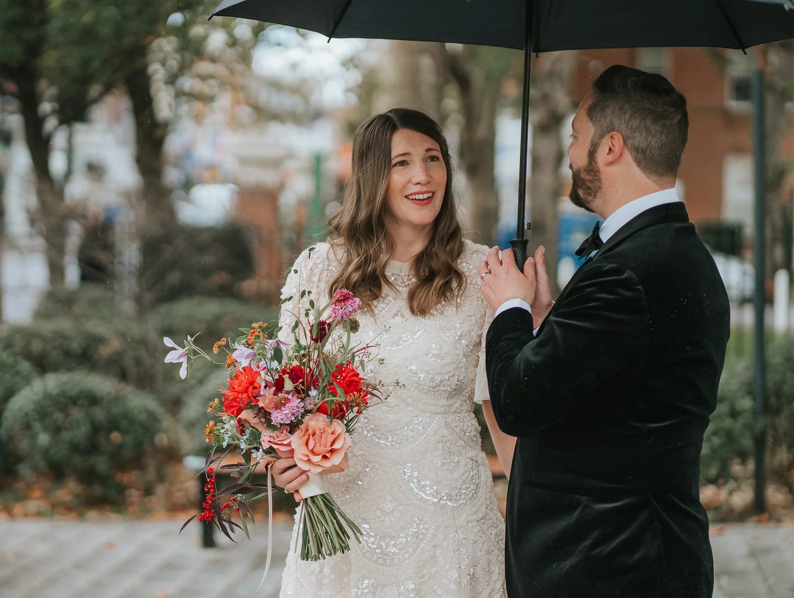  Bride and groom sharing a joyful moment under an umbrella outside Islington Town Hall, with the bride holding a vibrant, colourful bouquet. 