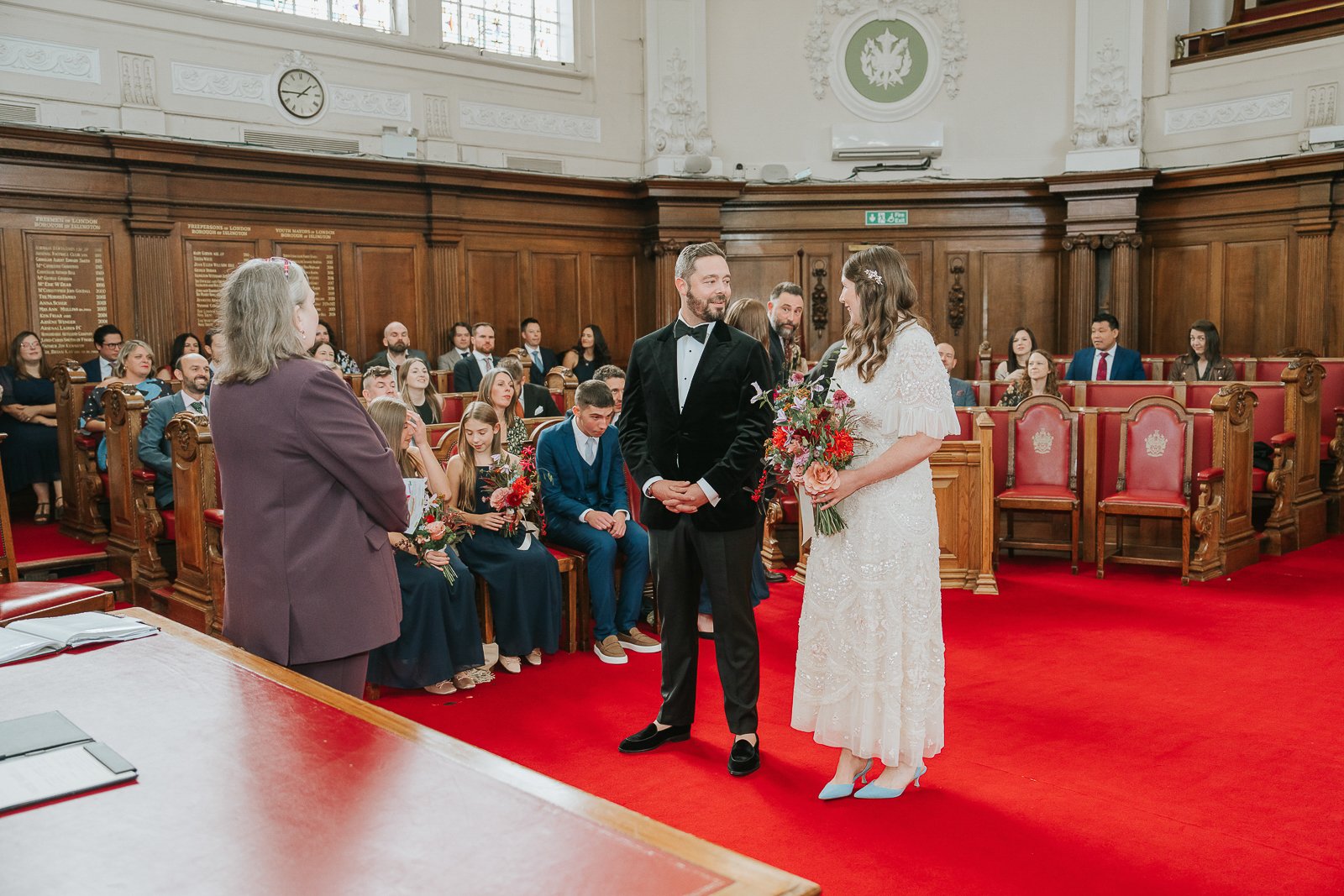  Bride and groom standing together during their Islington Town Hall wedding ceremony, smiling at each other while the registrar leads the vows. 