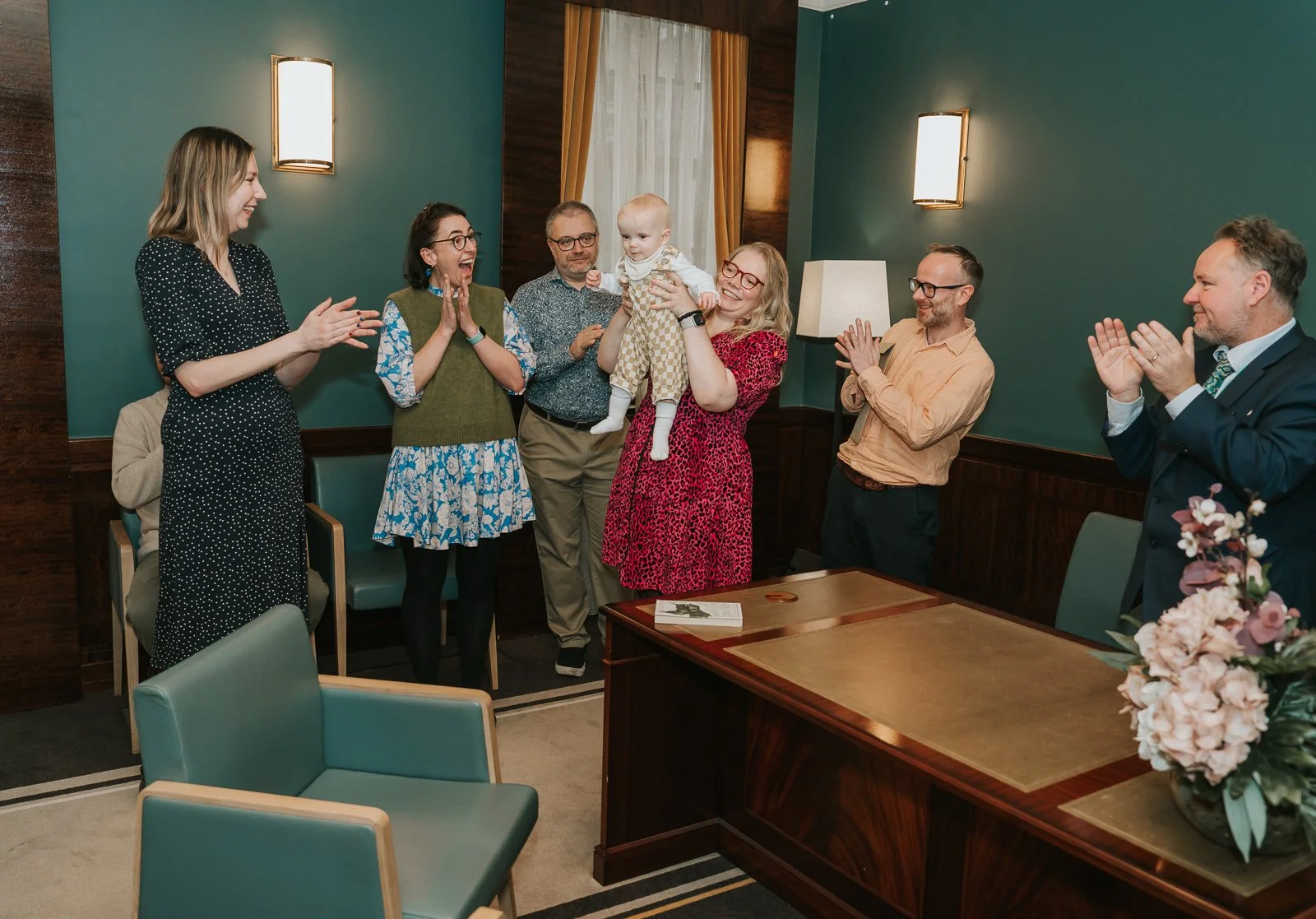  Celebratory moment as a parent lifts their baby proudly, surrounded by clapping guests and the registrar at Hackney Town Hall. 