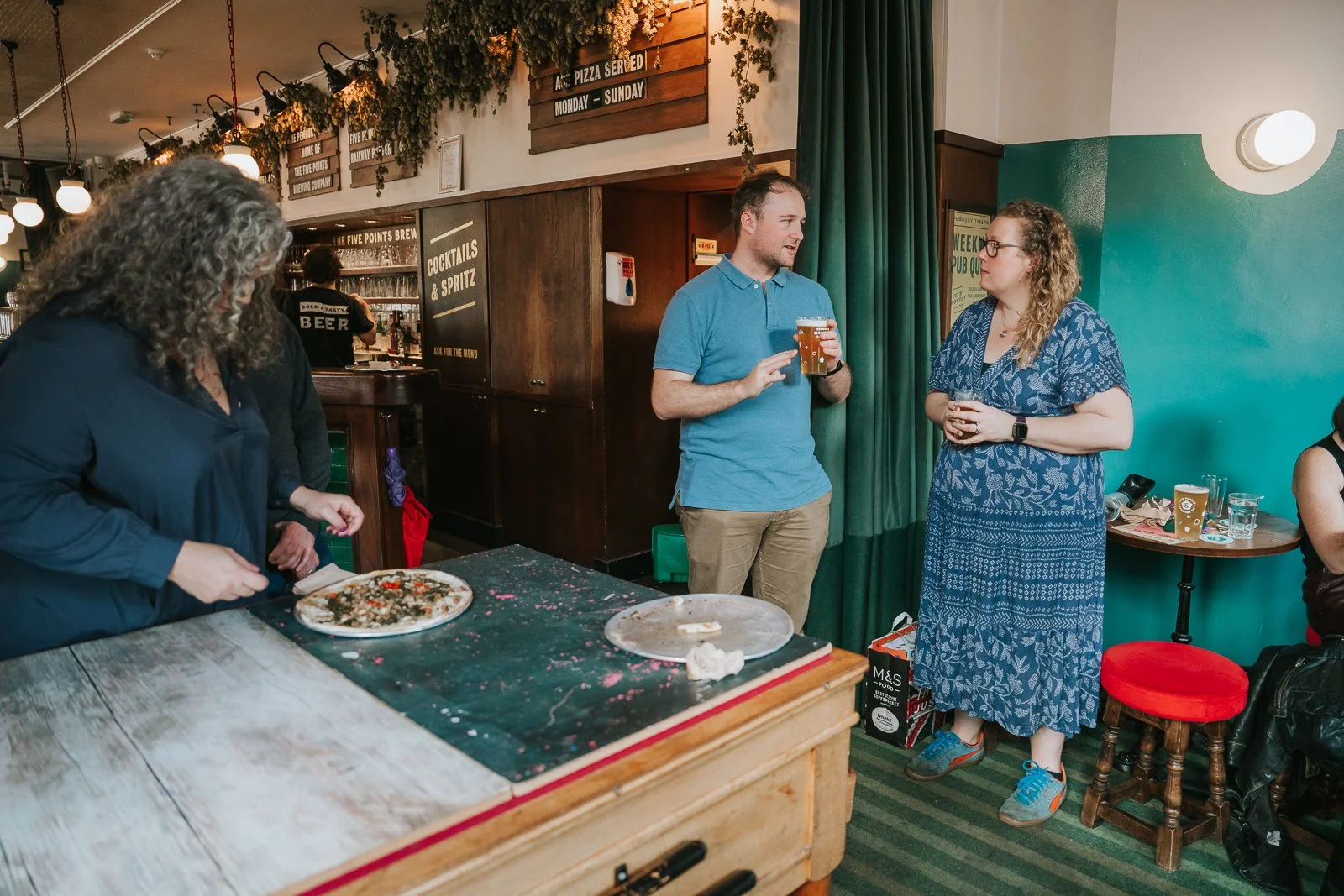  Guests standing and chatting near the bar at The Pembury Tavern as pizza is served on the pool table during the family celebration. 
