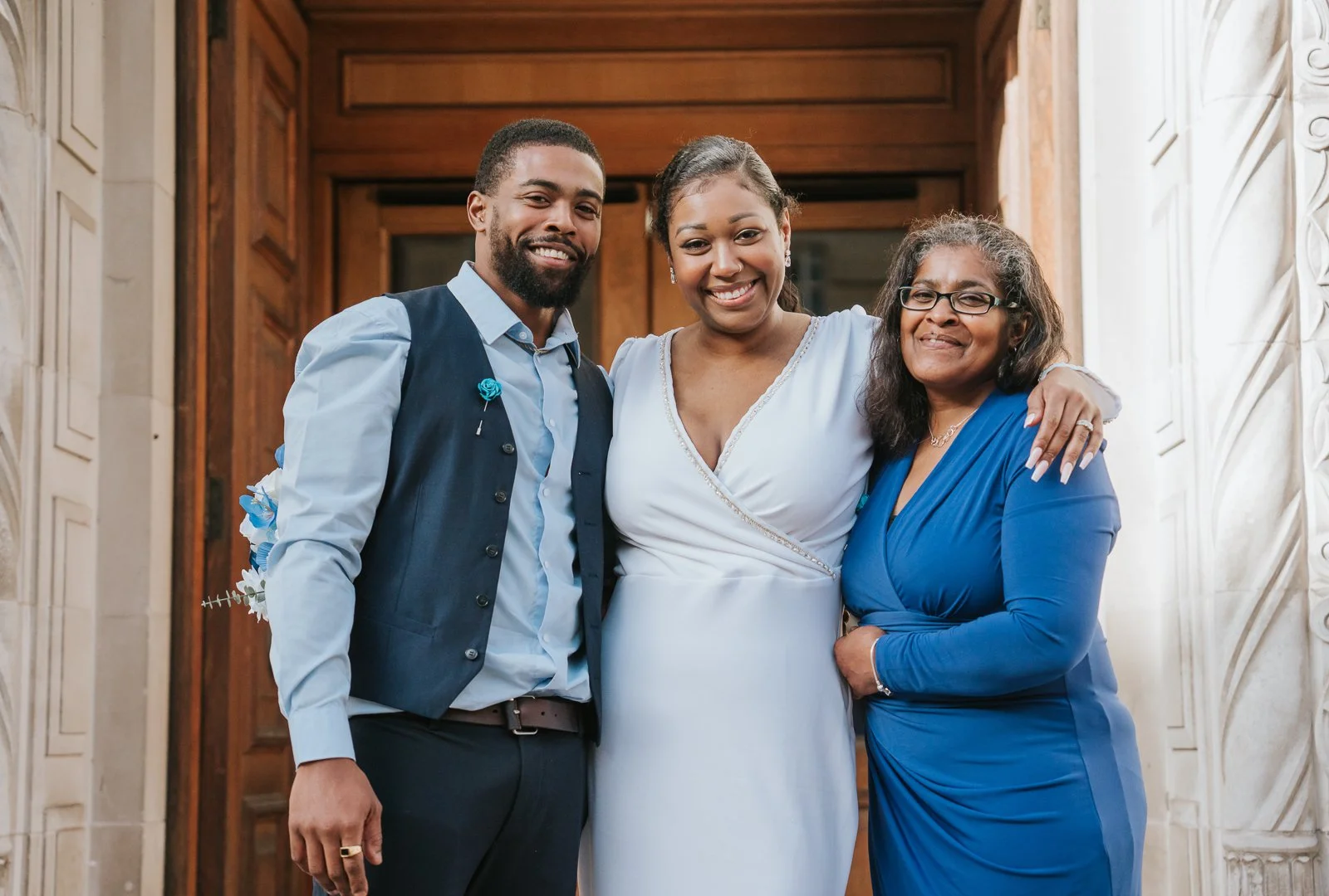  Bride standing arm-in-arm with two guests outside Wandsworth Town Hall, all smiling warmly for a relaxed family portrait. 