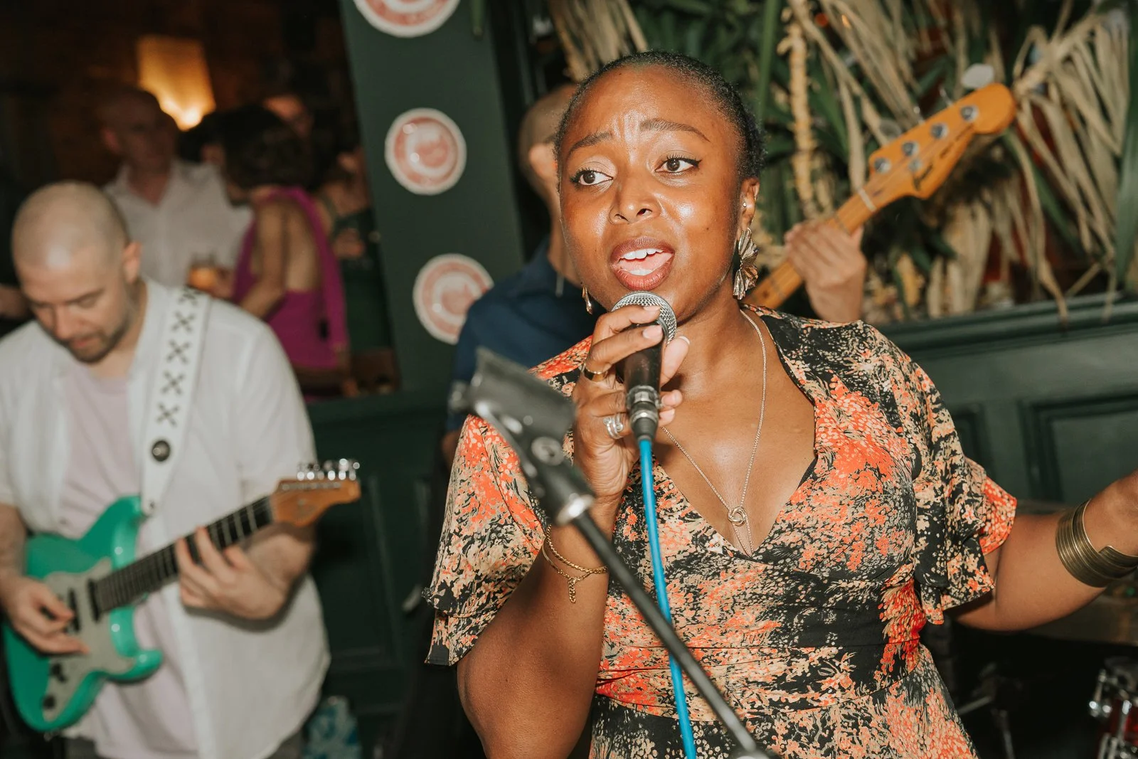  Close-up of a wedding band singer performing at a lively London pub reception, with musicians playing guitar and bass in the background. 