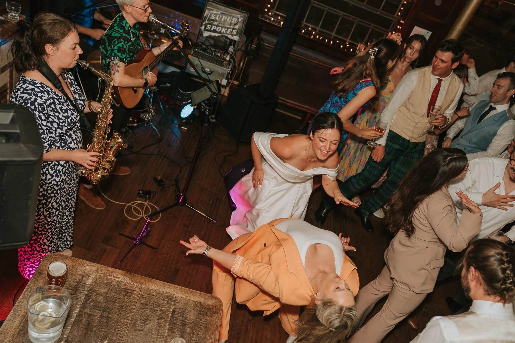  Bride and guests dancing energetically in front of a live wedding band at a London pub venue, with saxophone and guitar performances on stage. 