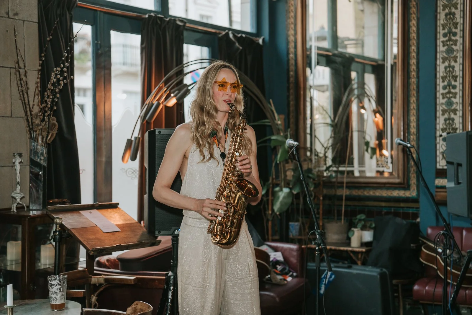  Female saxophonist performing at an intimate London pub wedding reception, surrounded by vintage décor and warm evening light. 