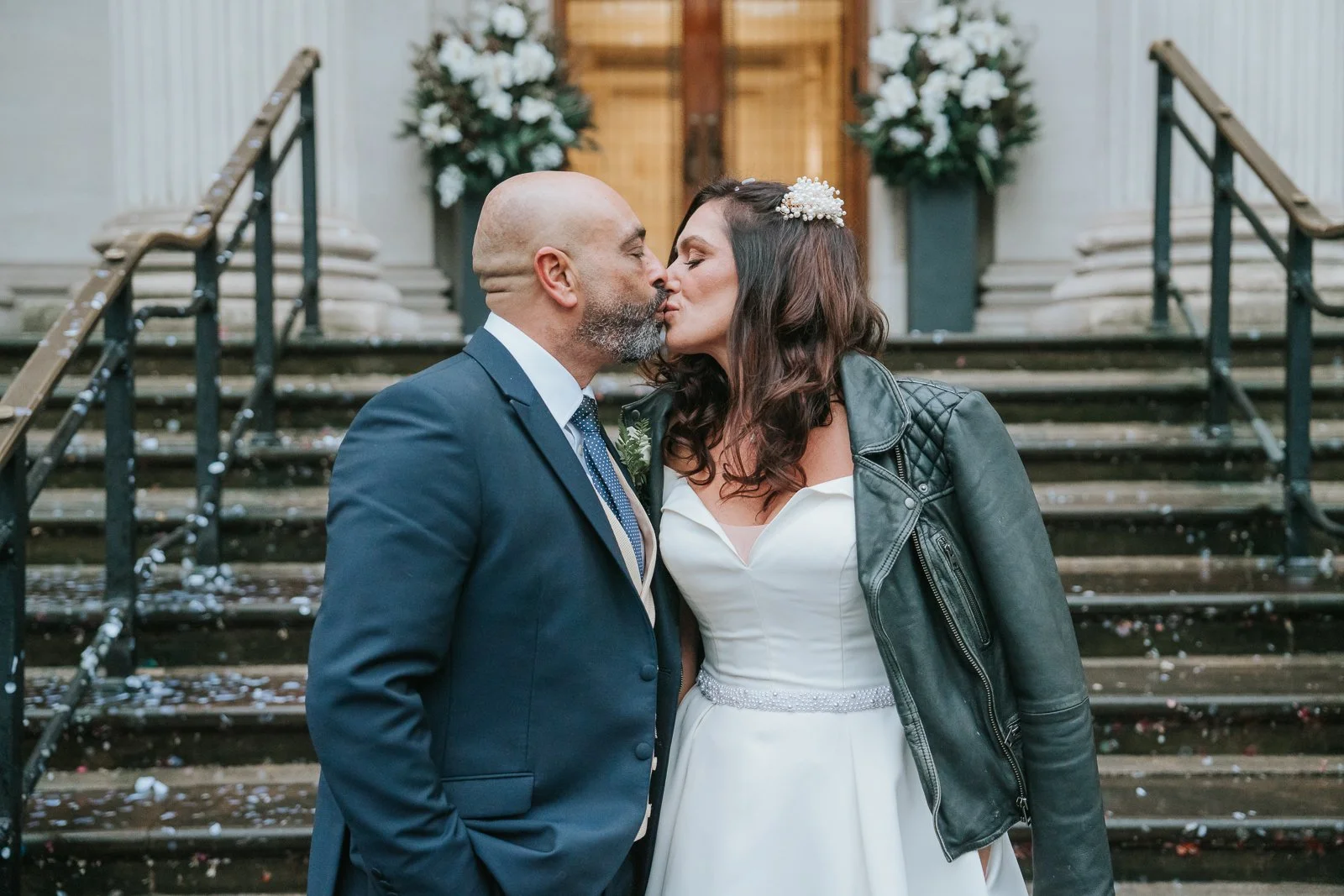  Bride and groom sharing a kiss on the steps of Marylebone Town Hall, surrounded by confetti just after their London registry office wedding ceremony. 