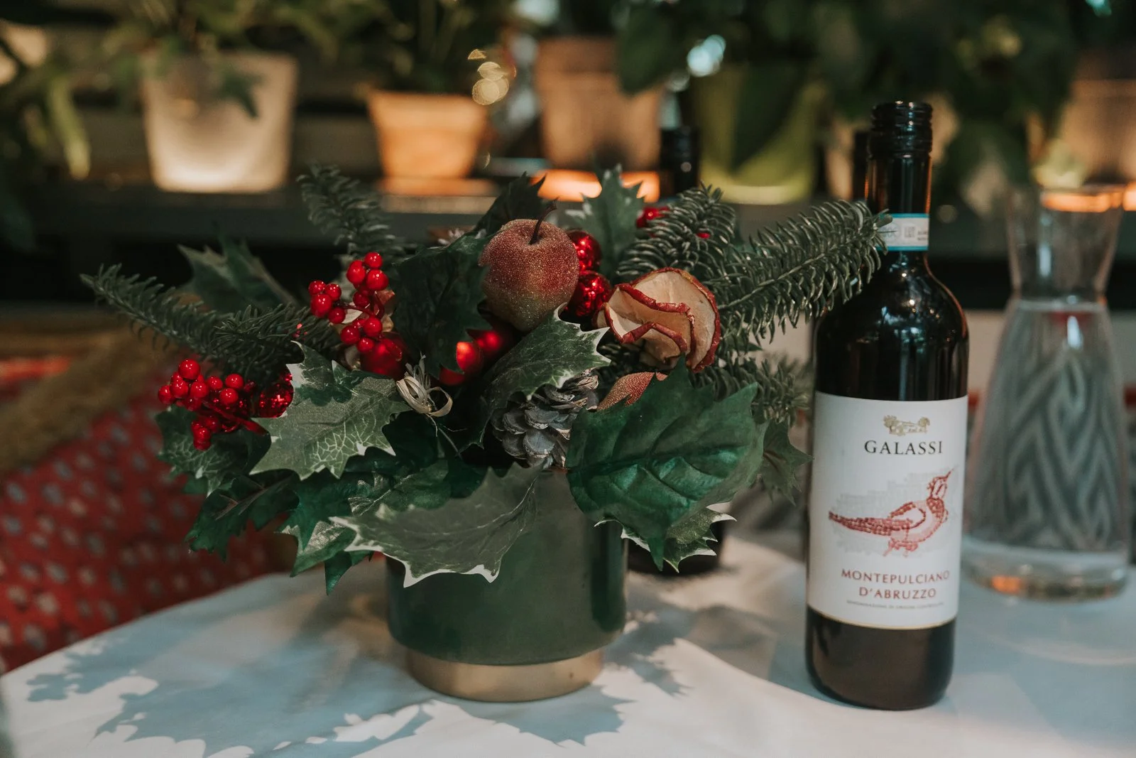  Christmas table styling in The Glasshouse Room at The Ivy Chelsea Garden, with seasonal greenery, holly, pinecones and festive décor alongside wine during a winter wedding reception in Chelsea 