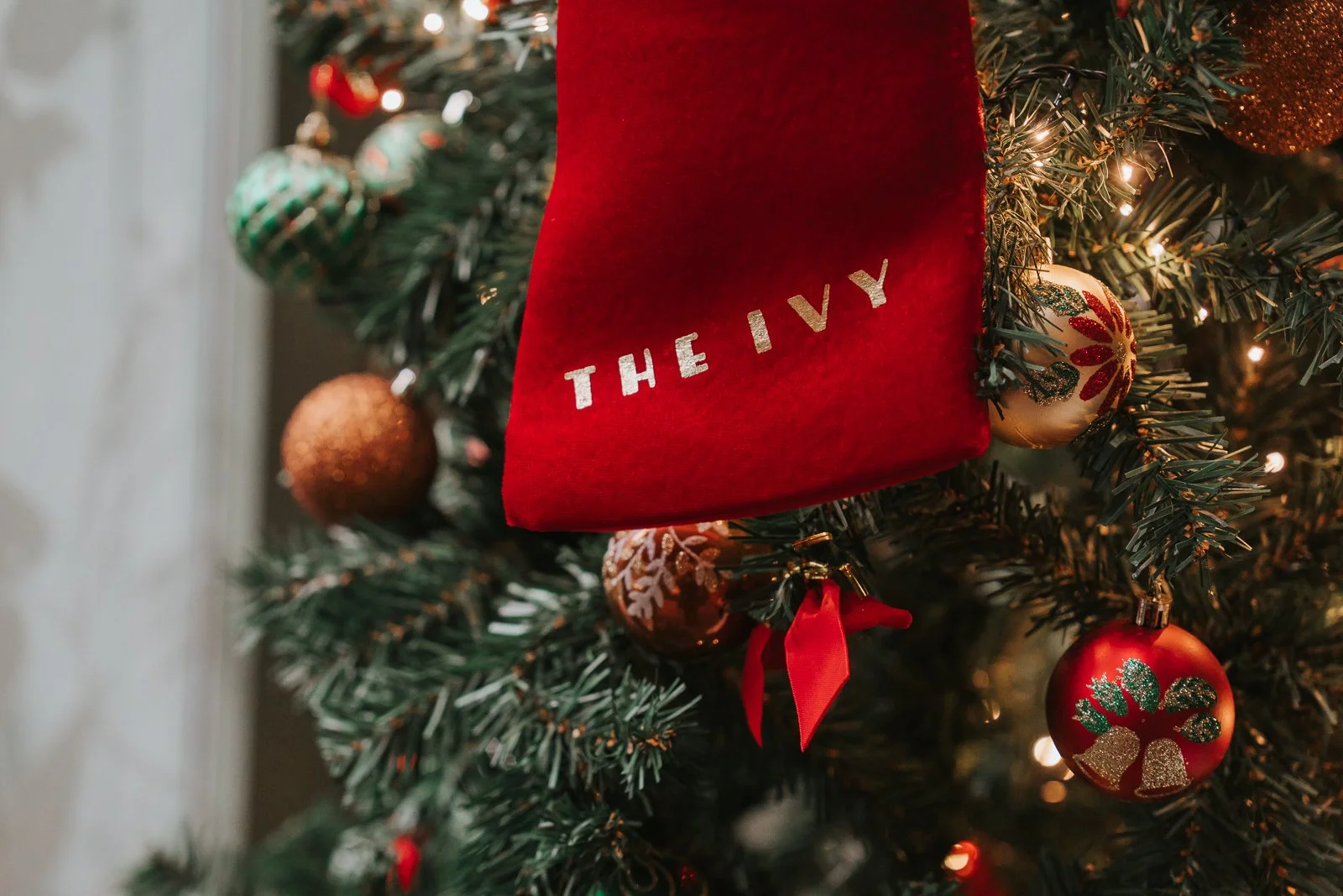  Festive Christmas details in The Glasshouse Room at The Ivy Chelsea Garden, featuring a decorated Christmas tree with red and gold baubles and a personalised Ivy stocking during an intimate Chelsea wedding celebration 