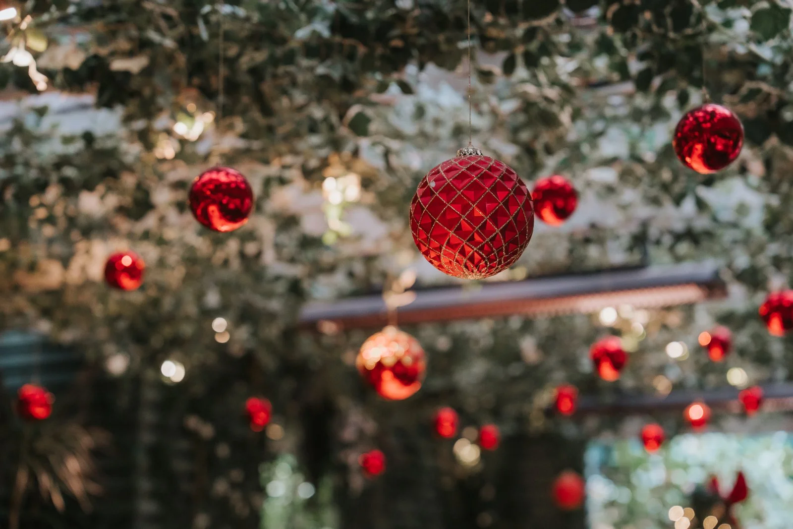  Festive Christmas decorations hanging from the ceiling in The Glasshouse Room at The Ivy Chelsea Garden, with red baubles and greenery creating a magical winter wedding atmosphere 