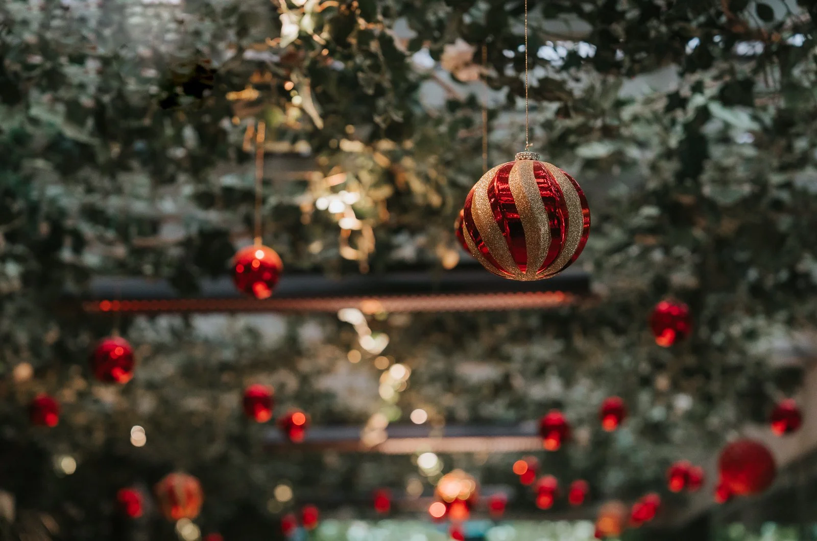  Festive Christmas decorations hanging from the ceiling in The Glasshouse  Room at The Ivy Chelsea Garden, with red baubles and greenery creating a magical winter wedding atmosphere 