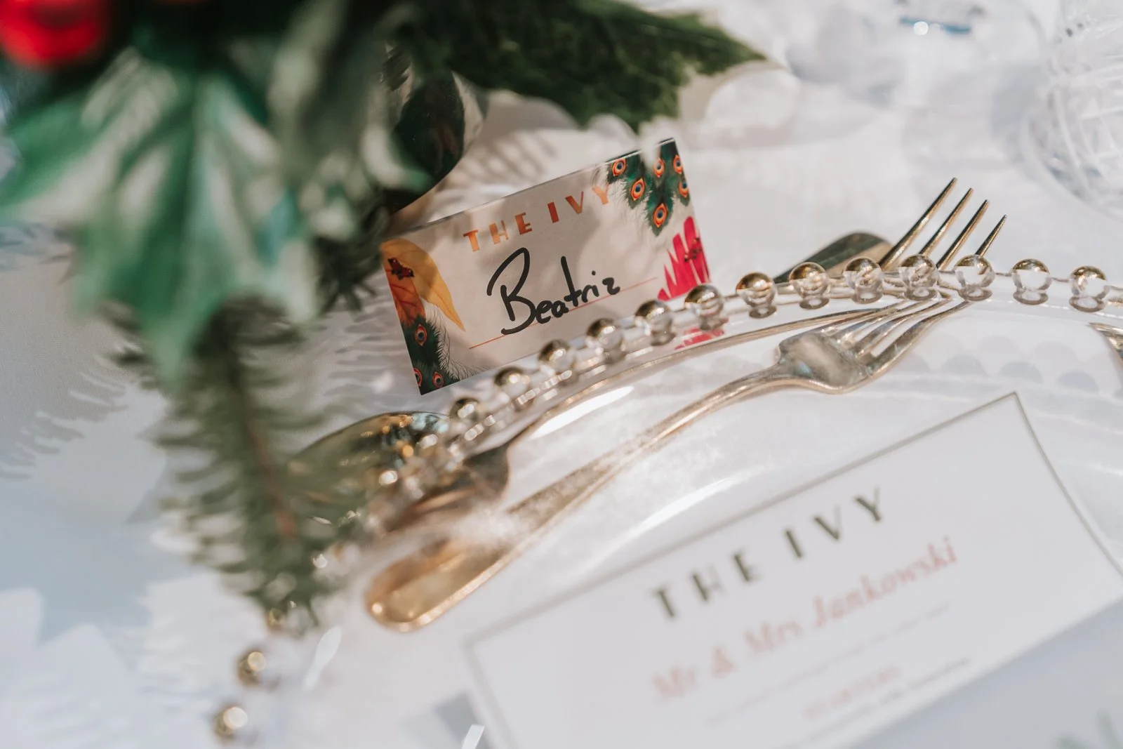  Personalised place card for the bride at a Christmas wedding reception in The Glasshouse  Room at The Ivy Chelsea Garden, styled with festive greenery and elegant cutlery 