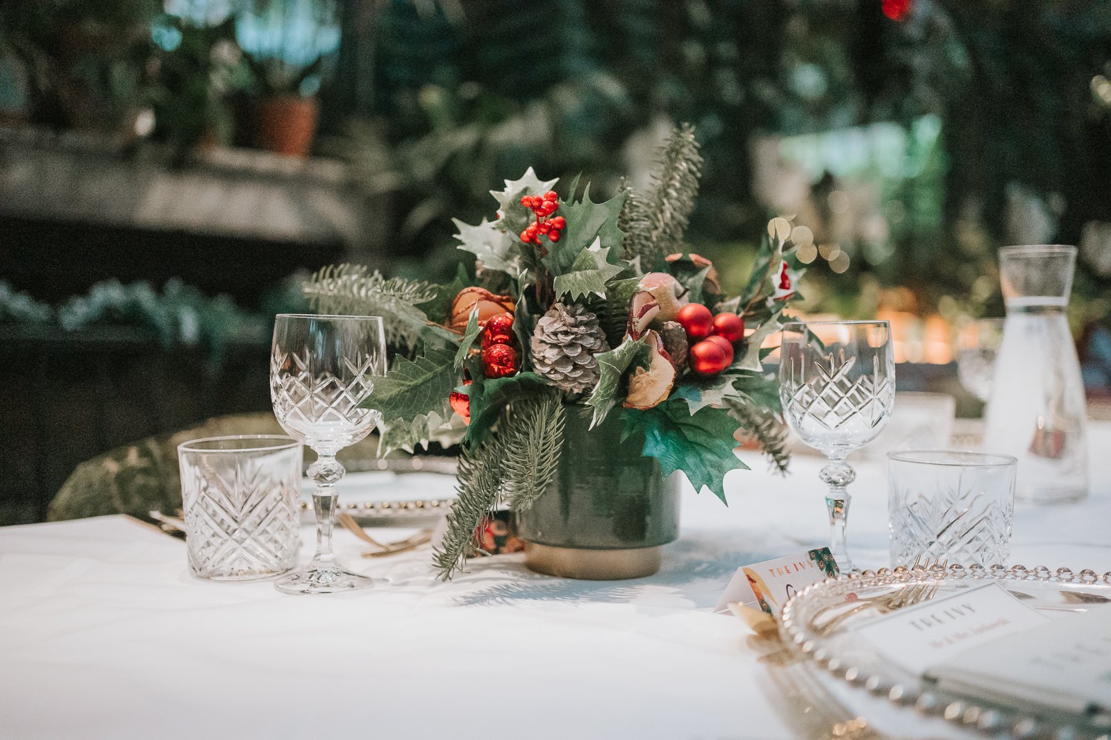  Festive table centrepiece with winter greenery, red berries and pinecones set on a wedding reception table in The Glasshouse  Room at The Ivy Chelsea Garden 