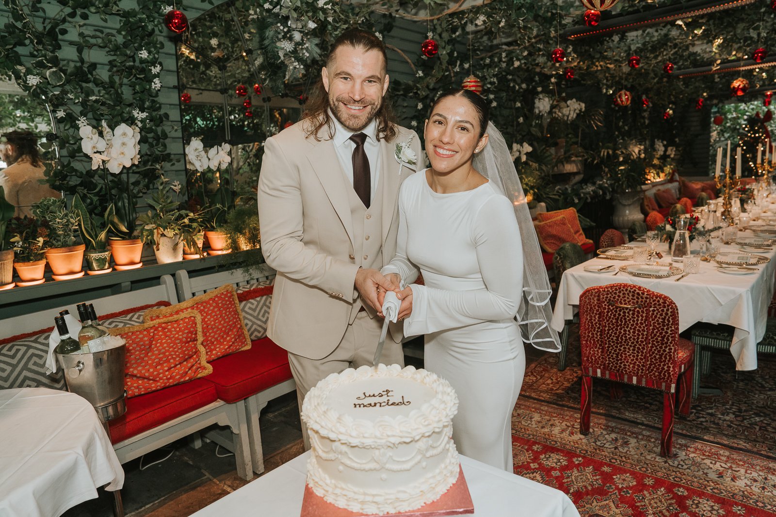  Bride and groom cutting their wedding cake in The Glasshouse Room at The Ivy Chelsea Garden, surrounded by festive Christmas décor and candlelit tables 