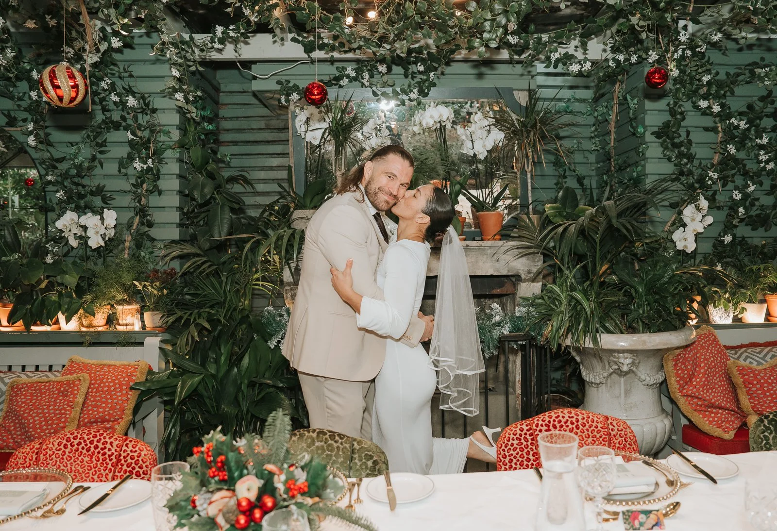  Bride and groom embracing beneath hanging greenery and Christmas decorations in the Glasshouse Room at The Ivy Chelsea Garden 
