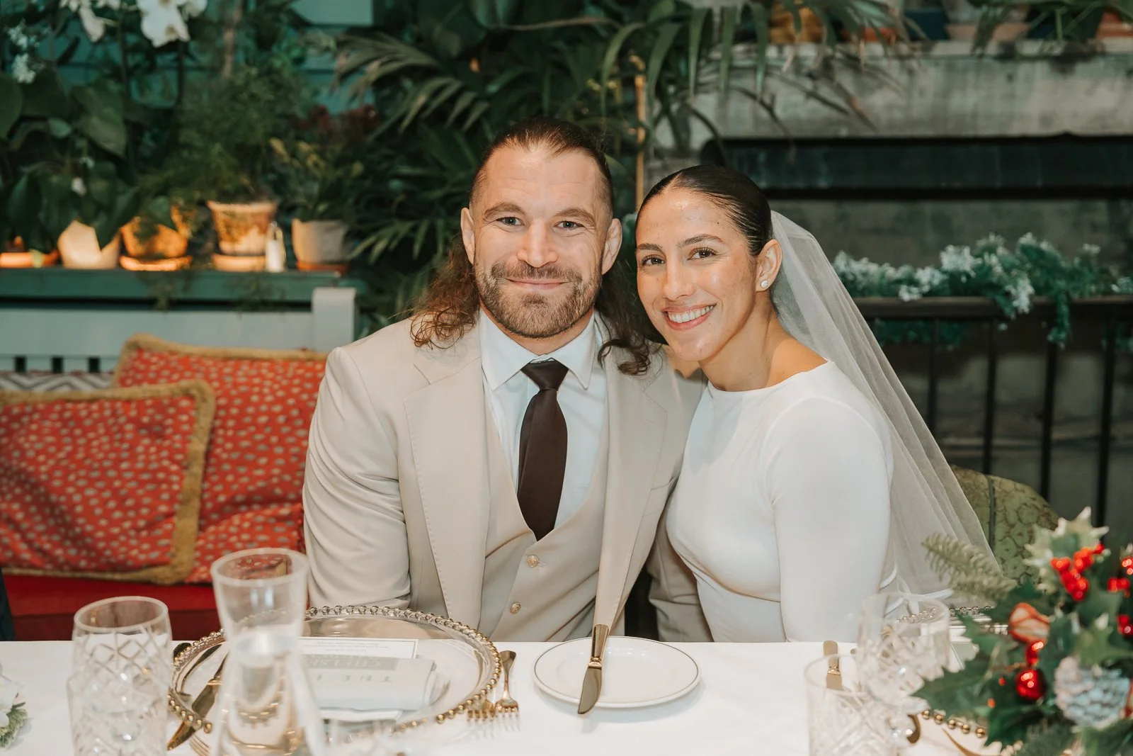  Close-up portrait of the bride and groom at their wedding reception table in the Glasshouse Room at The Ivy Chelsea Garden, styled with festive details 