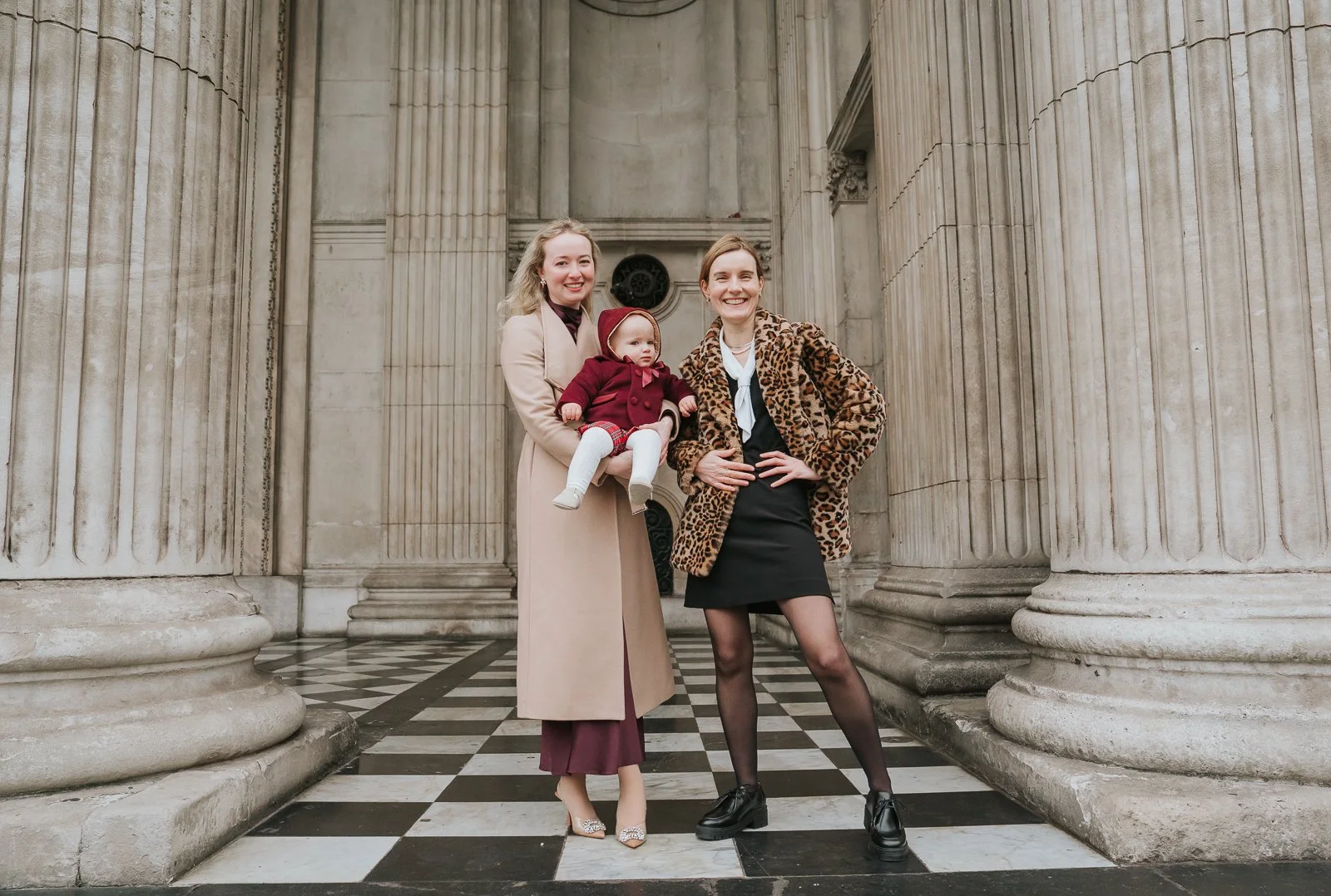  Relaxed family christening photo outside St Paul’s Cathedral, baby held between family members with classical columns behind 
