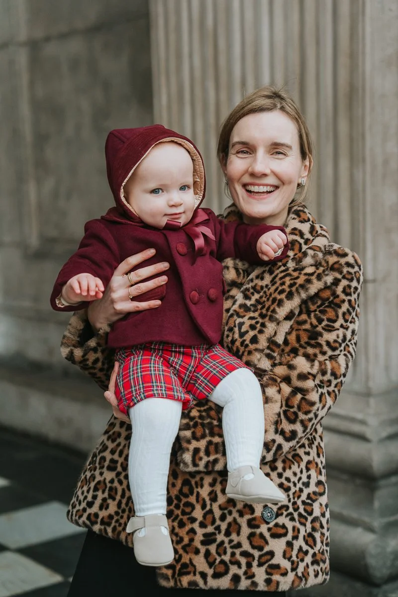  Godmother holding a baby outside St Paul’s Cathedral with stone columns in the background 