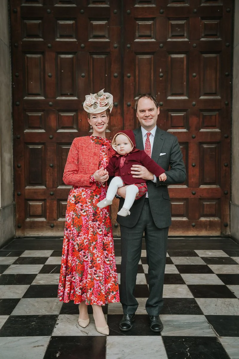  Parents and baby standing in front of the wooden doors at St Paul’s Cathedral after a christening 