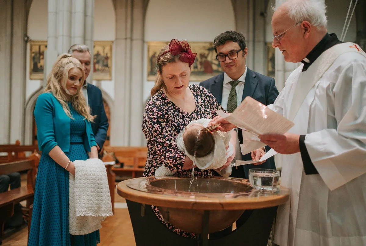  Priest pouring holy water over baby during Catholic christening ceremony as family and godparents look on in London church. 