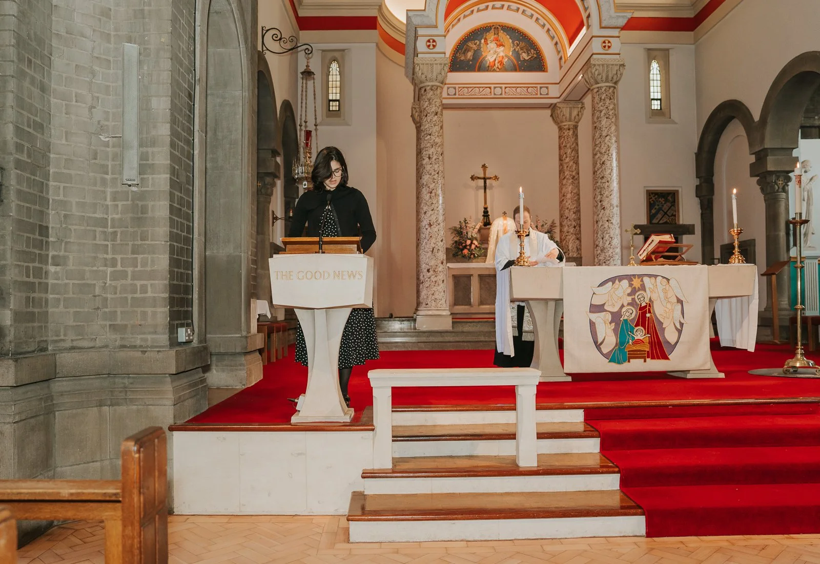  Family member reading from lectern during Catholic christening ceremony inside London church. 