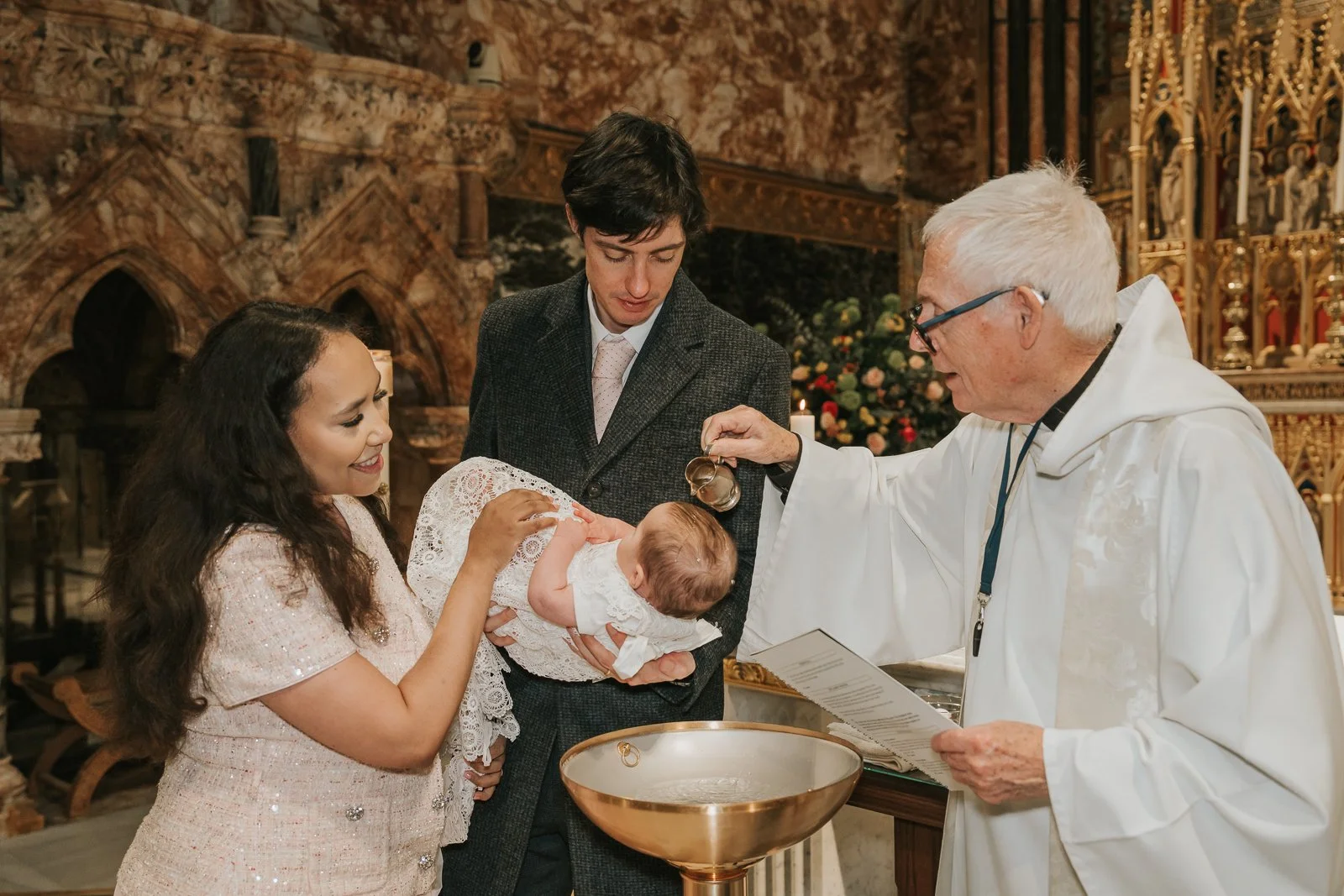  Priest pouring holy water over baby during Catholic baptism ceremony in London as parents look on. 