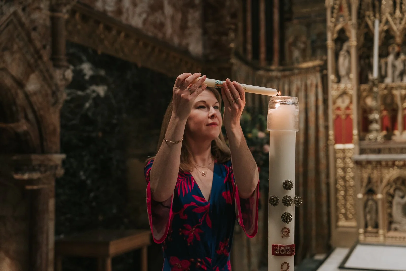  Godmother lighting baptism candle from Paschal candle during Catholic christening ceremony in London church. 