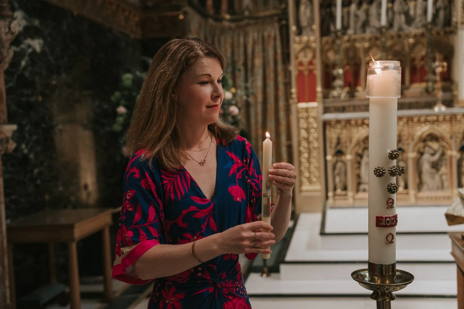  Godmother holding lit baptism candle beside Paschal candle following Catholic christening ceremony in London. 