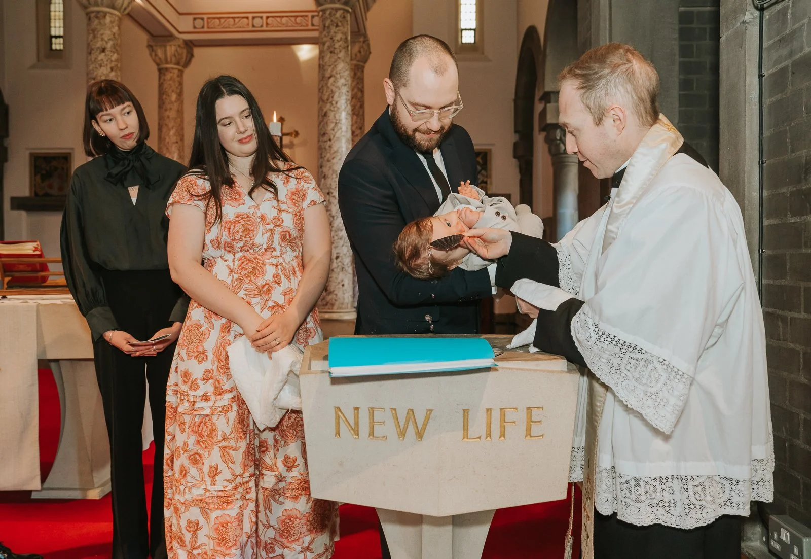  Priest pouring holy water over baby during Catholic baptism ceremony in London as parents look on. 
