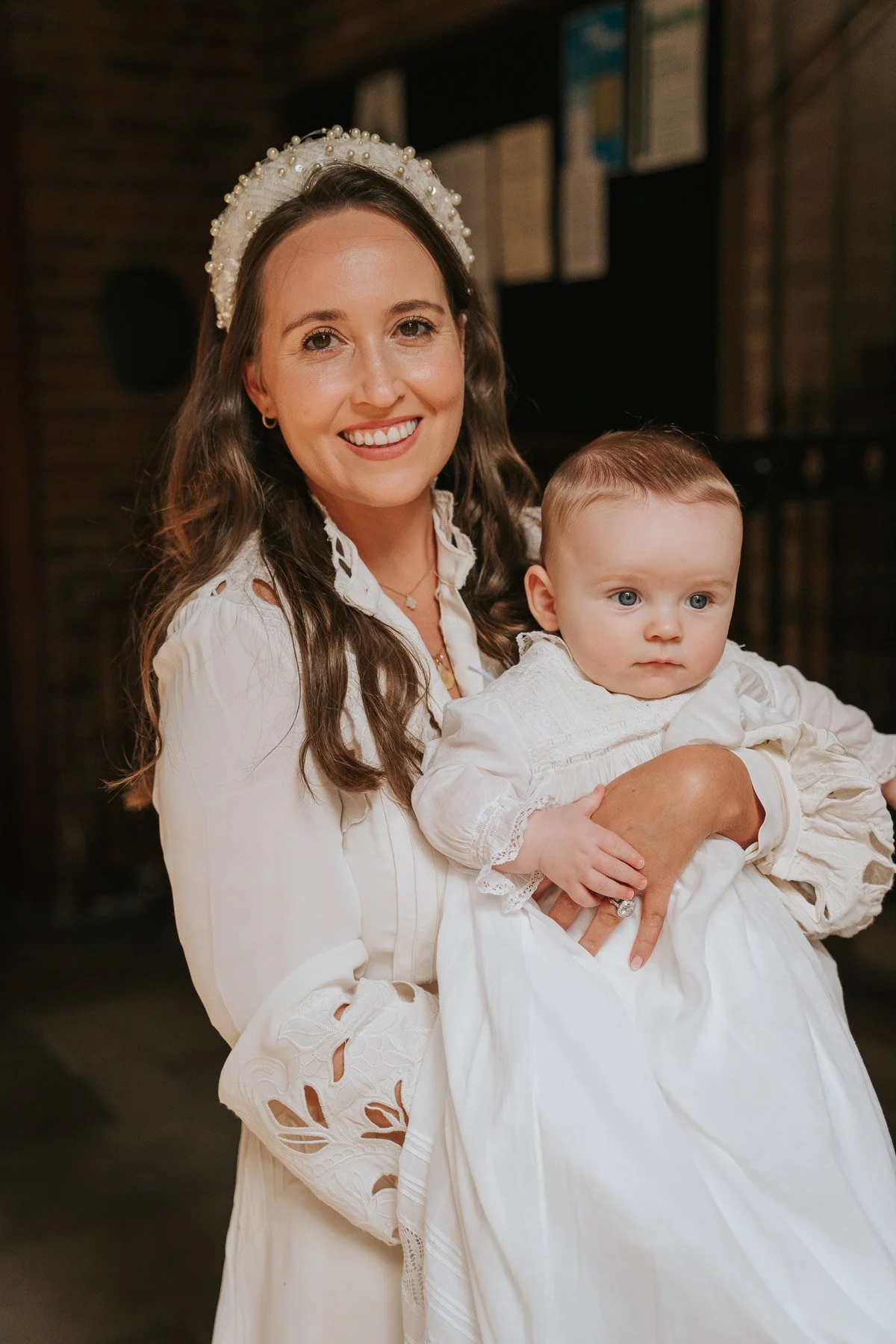  Mother holding baby in traditional christening gown inside London church after baptism ceremony. 