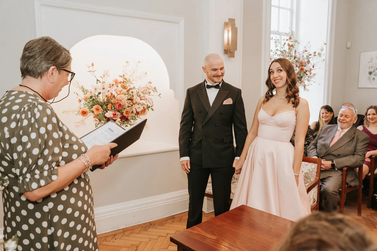  Civil ceremony taking place in the Rossetti Room at Chelsea Old Town Hall as the couple listen to the registrar during their London wedding. 