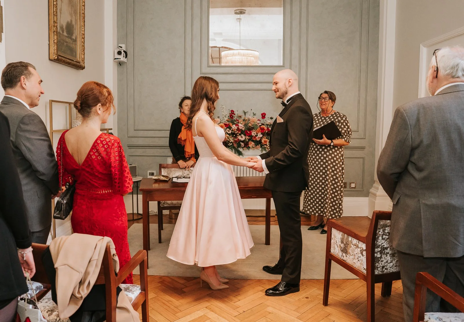  Couple holding hands during their Chelsea Old Town Hall wedding ceremony with guests seated around the intimate Rossetti Room. 