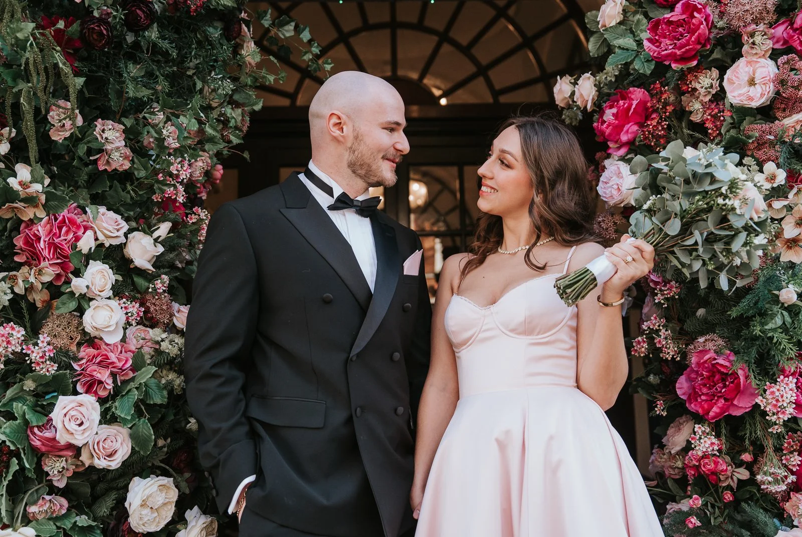  Newlyweds posing together outside after their intimate civil wedding ceremony with floral entrance backdrop. 