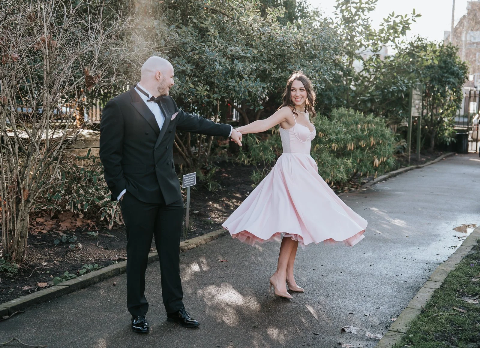  Bride twirling playfully while holding hands with her partner during relaxed post-ceremony portraits in a London garden. 