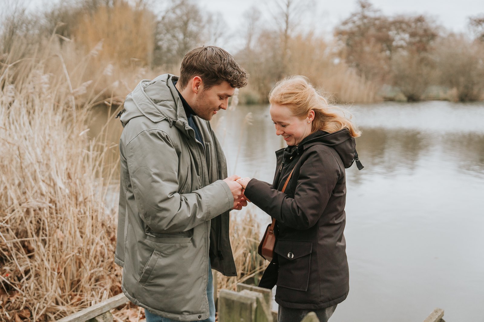  Man placing engagement ring on partner’s finger beside Clapham Common pond during intimate London proposal. 