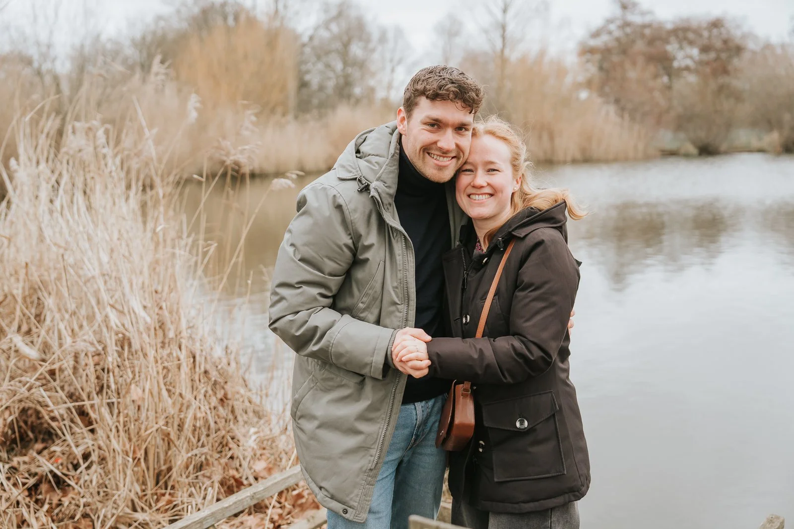  Just-engaged couple smiling at camera at Clapham Common lake after successful South London proposal. 