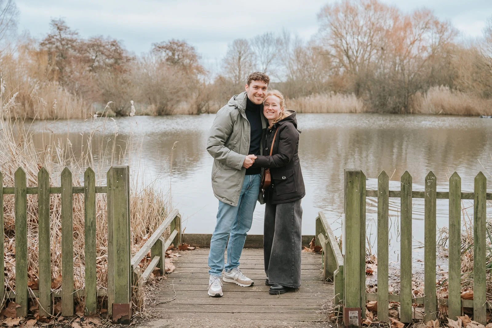  Engaged couple posing on jetty overlooking Clapham Common pond, quiet London proposal location. 