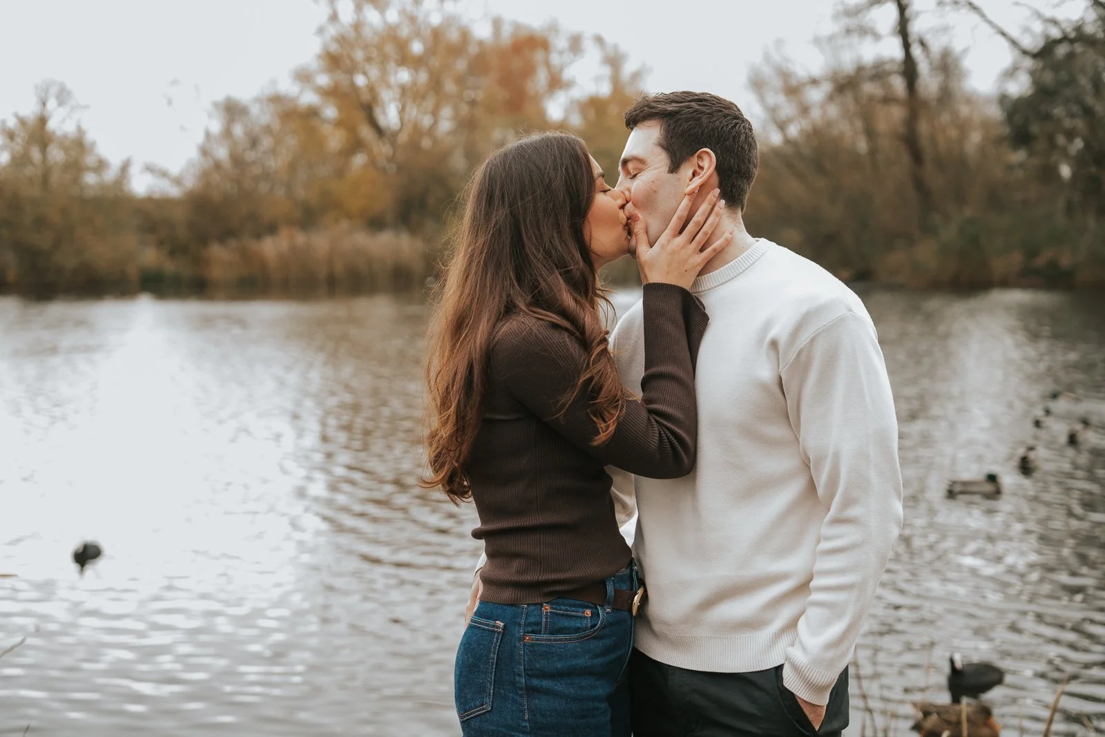  Couple kissing by the water at Clapham Common after a quiet outdoor proposal in London. 
