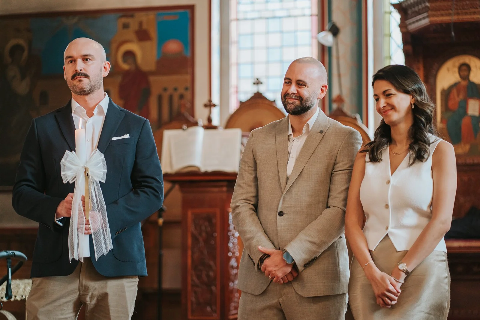  Parents and godfather standing during a Greek Orthodox christening ceremony at St Constantine &amp; St Helen Church in Crystal Palace, with icons and stained glass inside the South London church. 